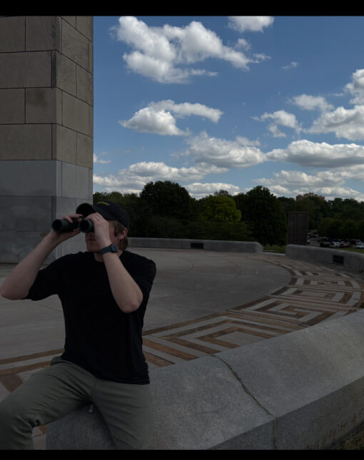 Man sitting outside on a concrete bench using an Oberwerk 8x32 SE binocular